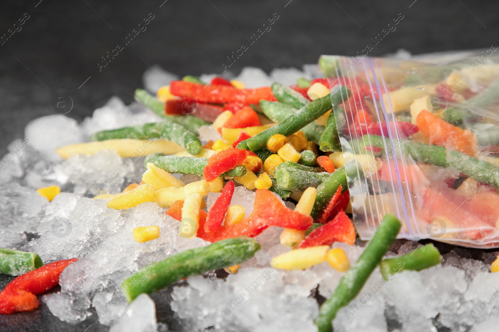 Photo of Zip bag with different frozen vegetables and ice on grey table, closeup