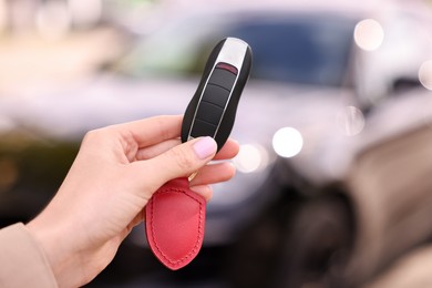 Woman holding car flip key near her vehicle outdoors, closeup