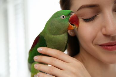 Young woman with cute Alexandrine parakeet on light background, closeup