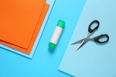 Photo of Glue stick, scissors and colorful paper on light blue background, flat lay