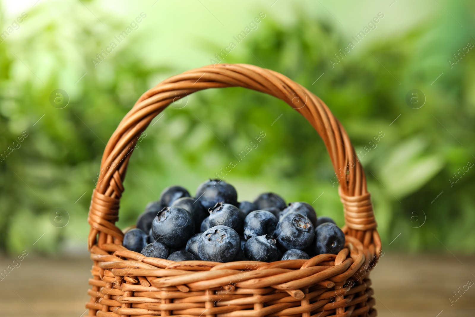 Photo of Tasty ripe blueberries in wicker basket on blurred green background