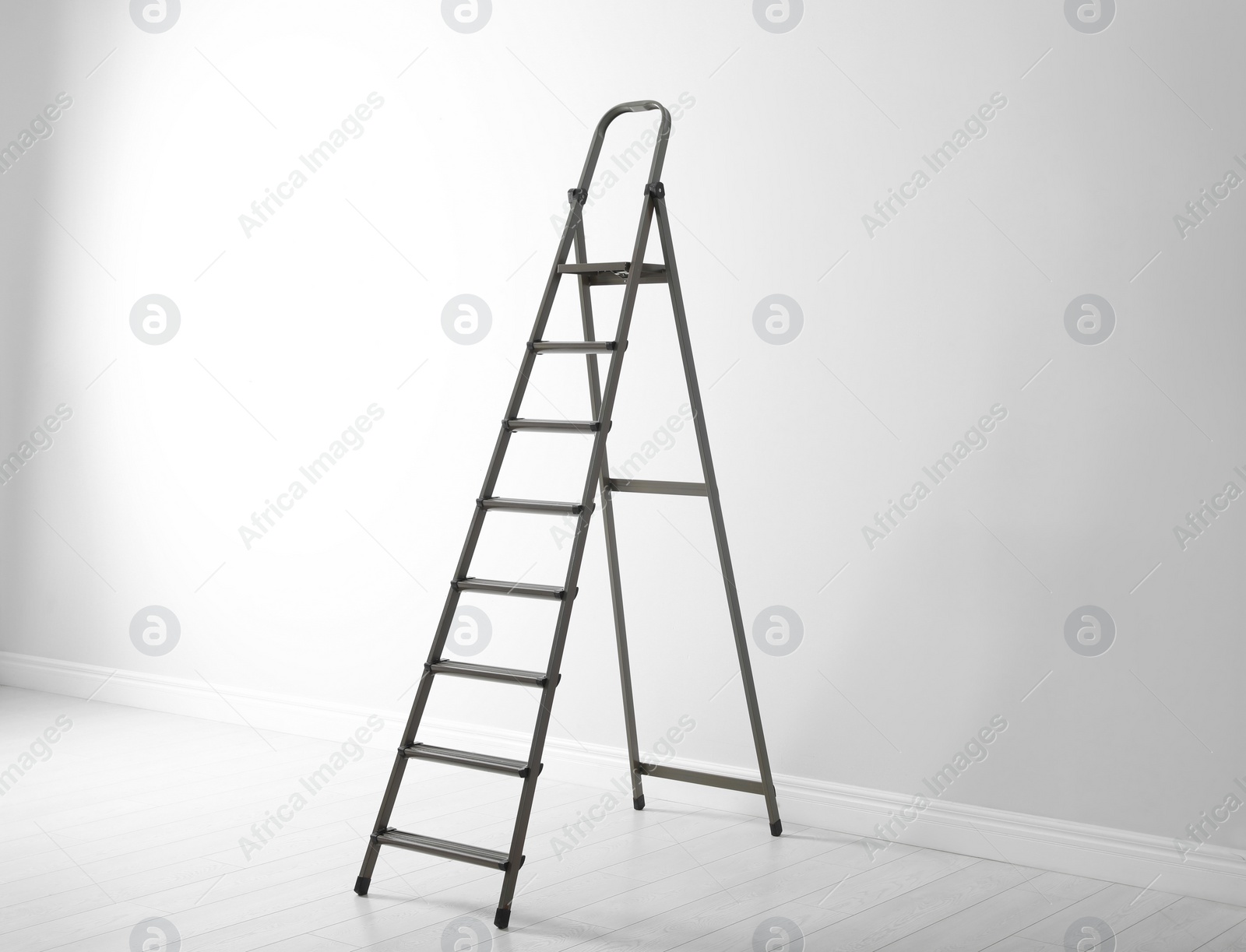 Photo of Modern metal stepladder near white wall indoors