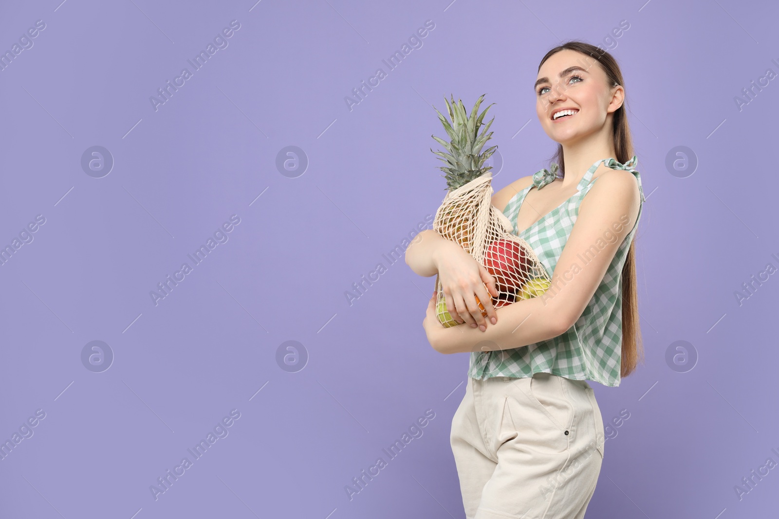 Photo of Woman with string bag of fresh fruits on violet background, space for text