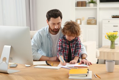 Photo of Father spending time with his son at desk. Taking break in remote work at home
