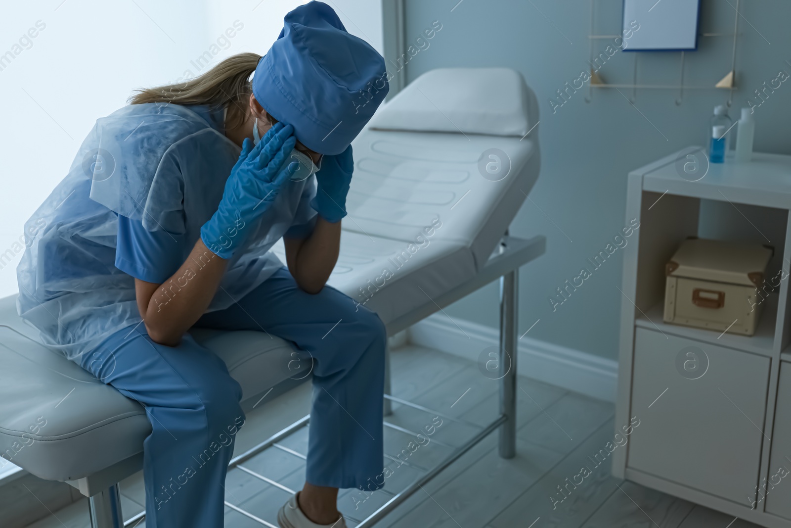 Photo of Exhausted doctor sitting on examination table in office. Stress of health care workers during COVID-19 pandemic