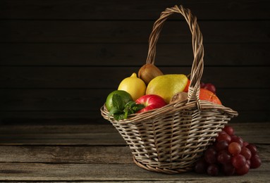 Photo of Fresh ripe fruits in wicker basket on wooden table, space for text