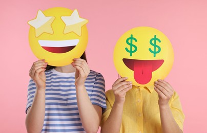 People covering faces with emoticons on pink background