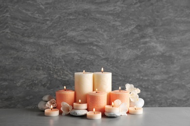 Beautiful composition with candles, flowers and stones on table against grey background. Space for text