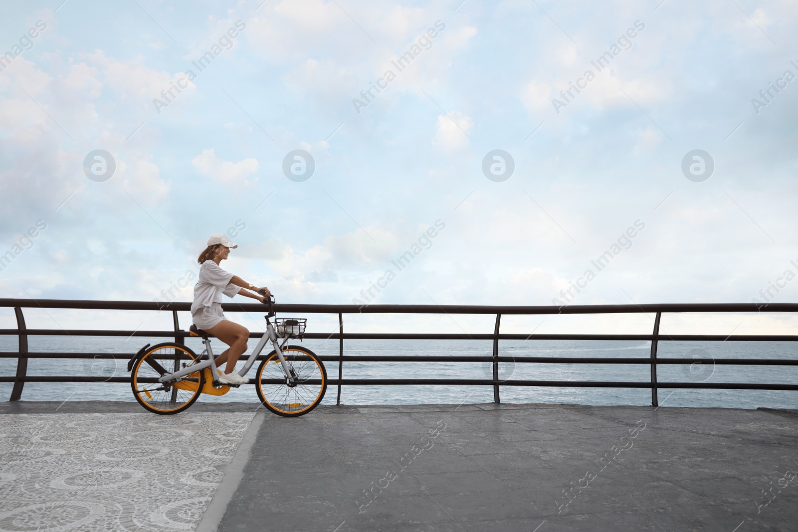 Photo of Beautiful young woman riding bicycle along embankment. Space for text