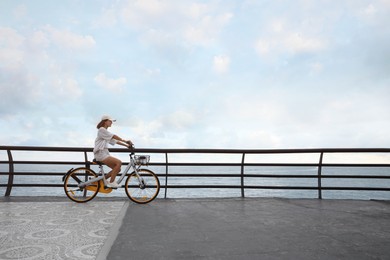 Beautiful young woman riding bicycle along embankment. Space for text