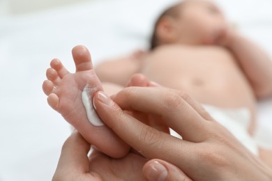 Photo of Mother applying body cream onto feet of her little baby, closeup