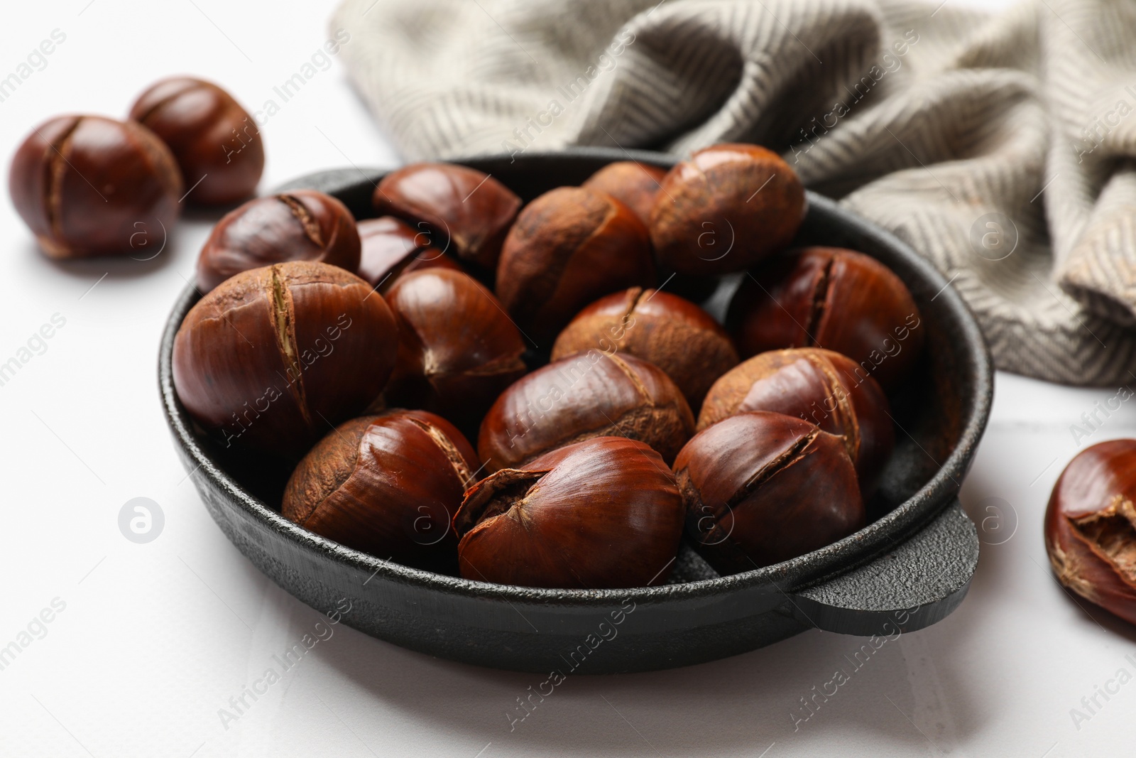 Photo of Fresh edible sweet chestnuts in frying pan on white tiled table, closeup