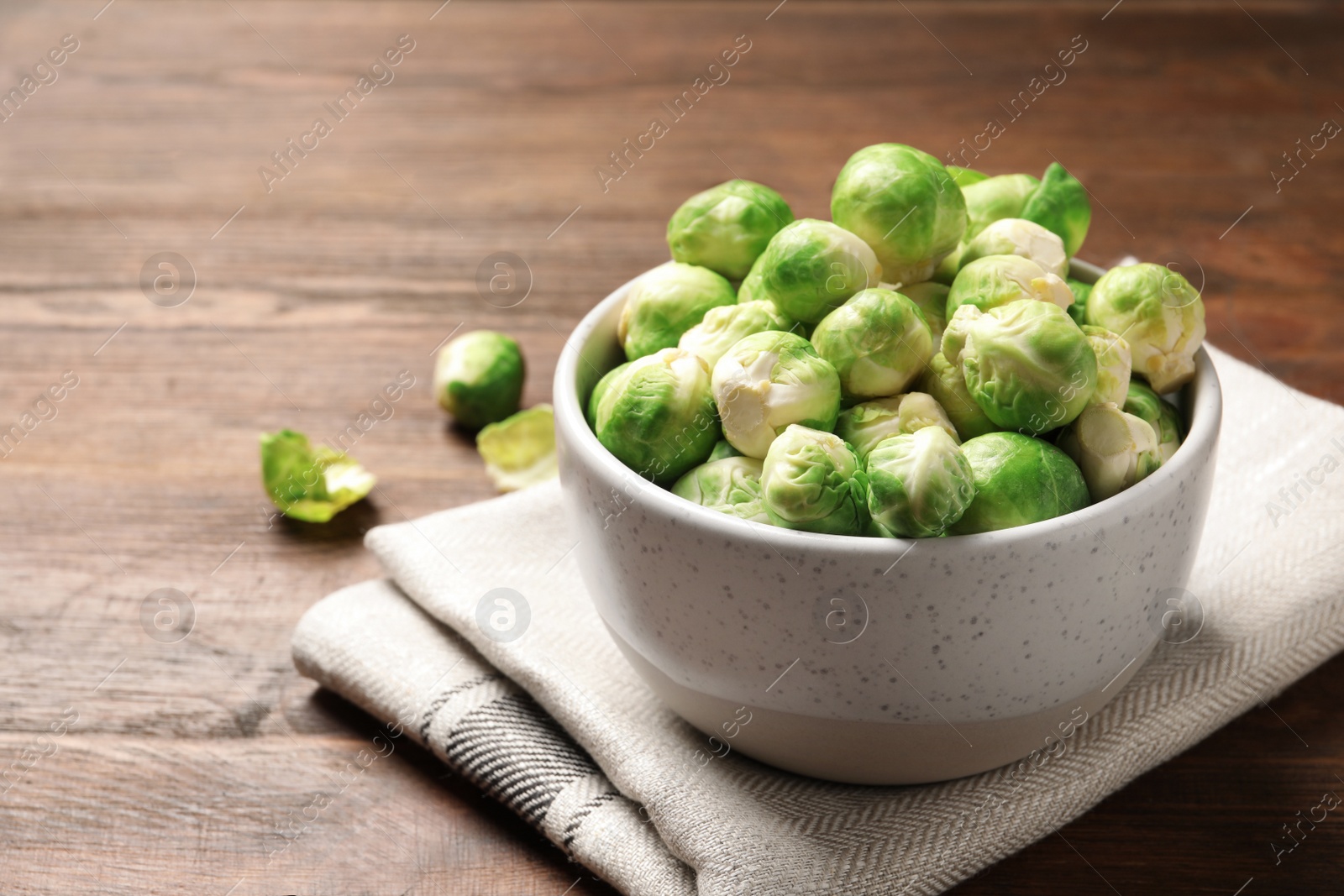 Photo of Bowl of fresh Brussels sprouts and napkin on wooden table. Space for text