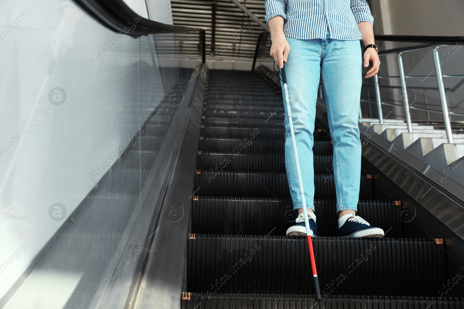 Photo of Blind person with long cane on escalator indoors