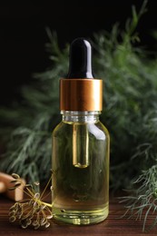 Photo of Bottle of essential oil and fresh dill on wooden table