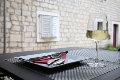 Plate, napkin, cutlery and glass of wine on black table outdoors