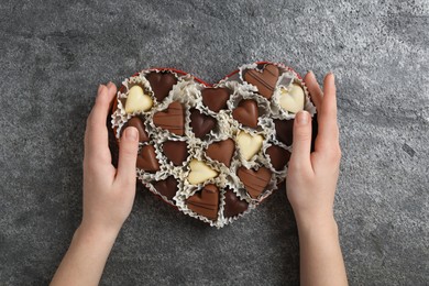 Photo of Woman with box of heart shaped chocolate candies at grey table, top view