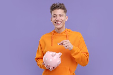 Photo of Happy man putting coins into piggy bank on purple background