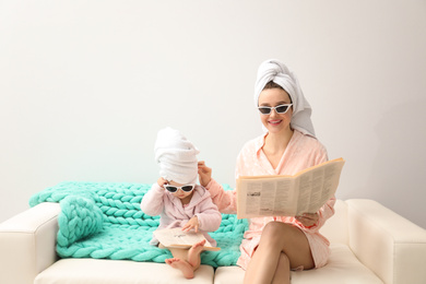 Photo of Mother and little daughter in bathrobes with newspapers sitting on sofa