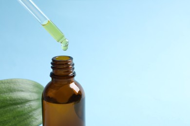 Photo of Dripping cosmetic oil from pipette into bottle on light blue background, closeup. Space for text