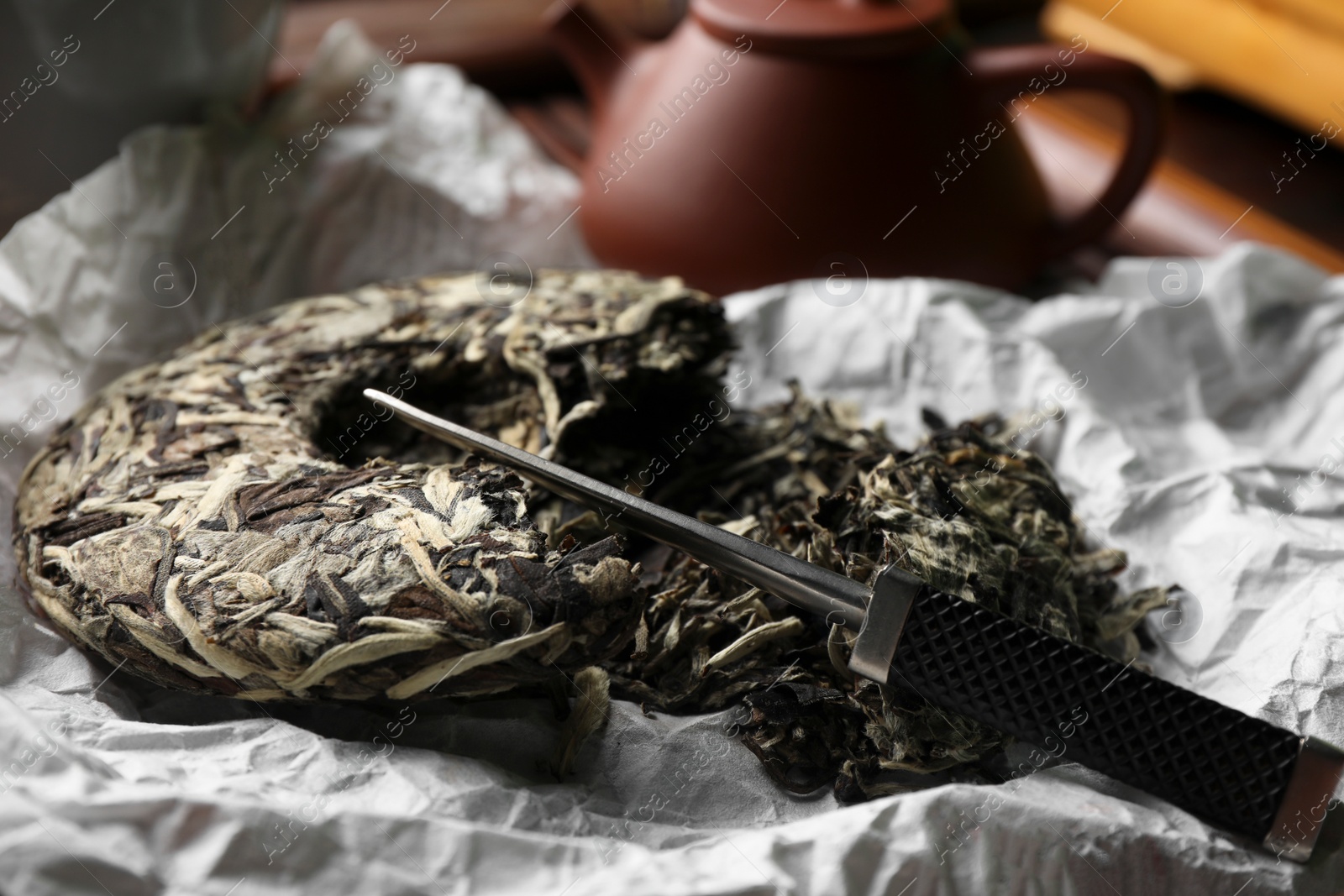 Photo of Broken disc shaped pu-erh tea and knife on parchment paper, closeup. Traditional ceremony