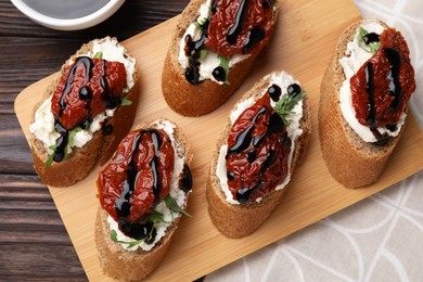 Photo of Delicious bruschettas with sun-dried tomatoes, cream cheese and balsamic vinegar on wooden table, flat lay
