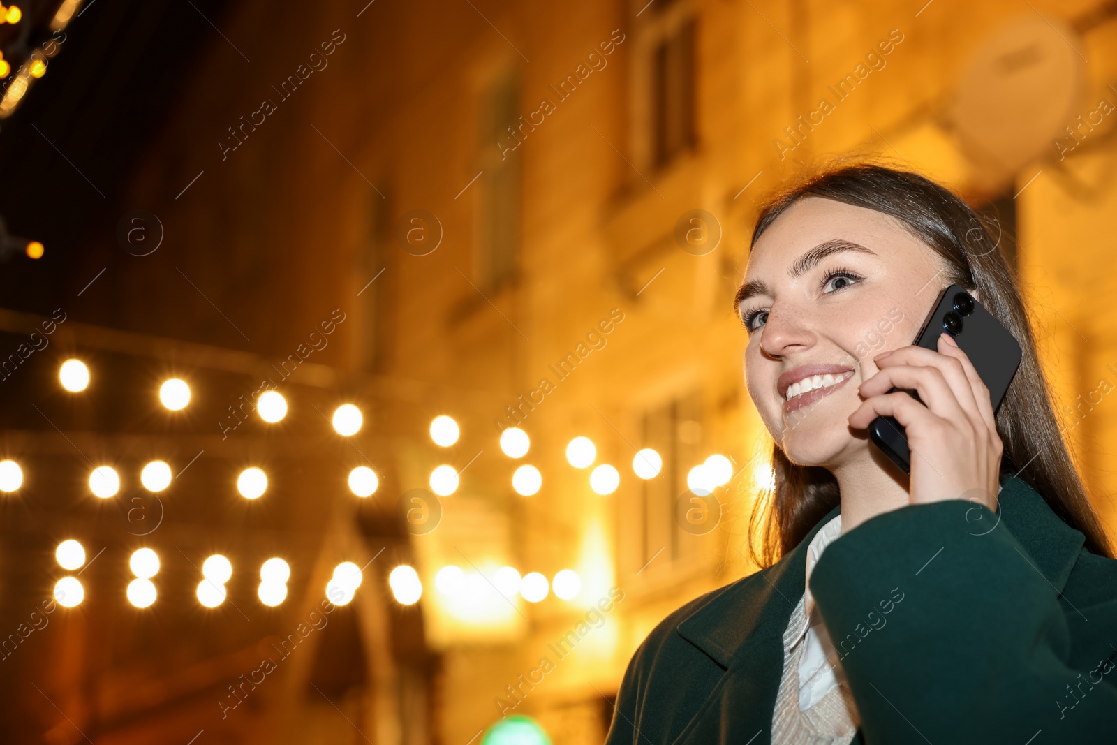 Photo of Smiling woman talking by smartphone on night city street. Space for text