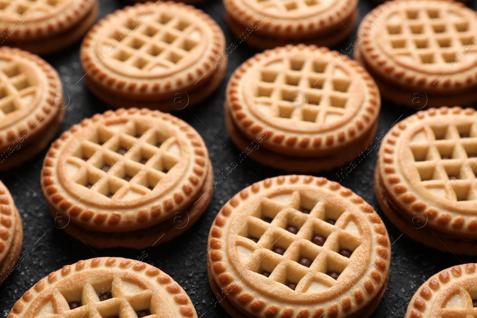 Photo of Tasty sandwich cookies with cream on black textured background, closeup