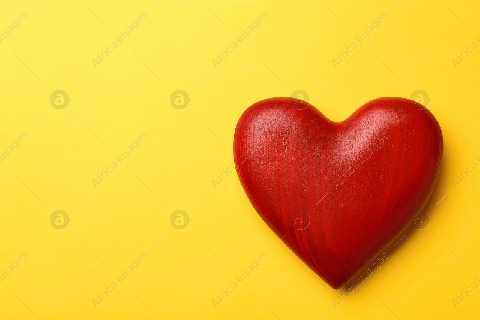 Photo of Red wooden heart on yellow background, top view. Space for text