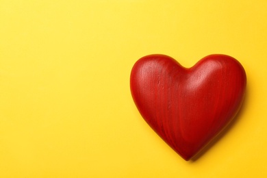 Photo of Red wooden heart on yellow background, top view. Space for text