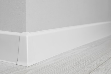 White plinth with connector on laminated floor near wall indoors, closeup
