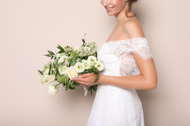 Young bride wearing wedding dress with beautiful bouquet on beige background, closeup