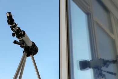 Tripod with modern telescope near open window indoors, low angle view. Space for text