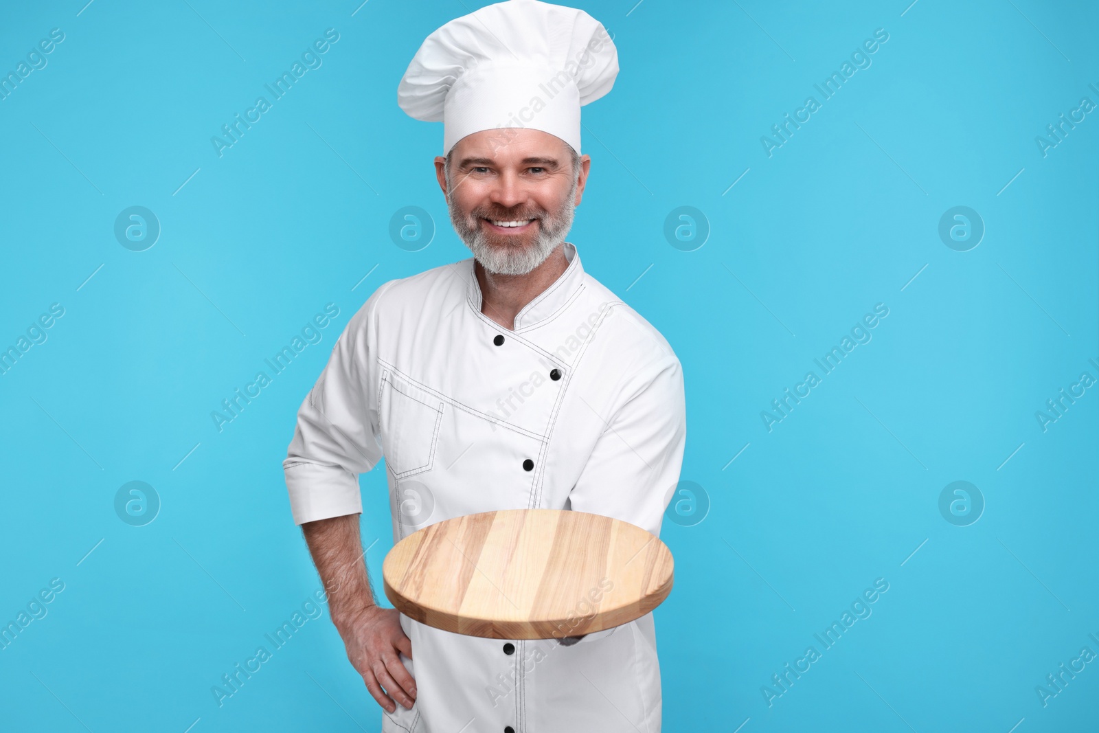 Photo of Happy chef in uniform with wooden board on light blue background