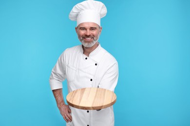 Photo of Happy chef in uniform with wooden board on light blue background