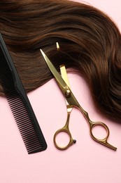 Photo of Professional hairdresser scissors and comb with brown hair strand on pink background, top view