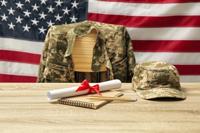 Photo of Diploma, stationery and soldier uniform near flag of United States. Military education