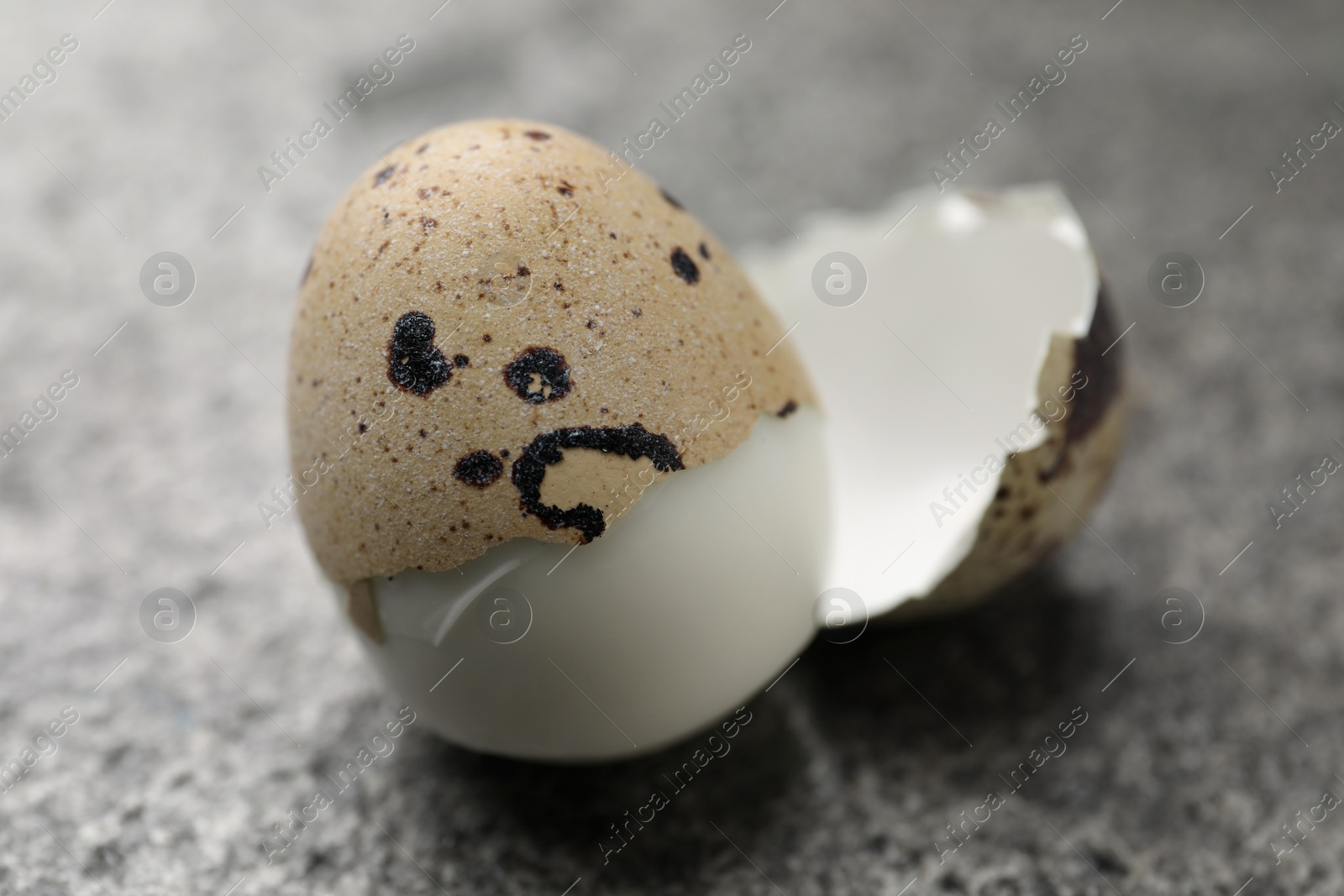 Photo of Boiled quail egg partly in shell on grey table, closeup