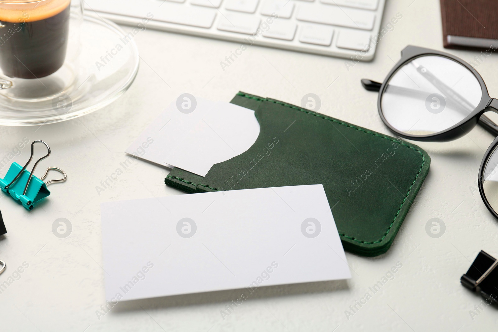 Photo of Leather business card holder with blank cards, glasses, keyboard and stationery on white table, closeup