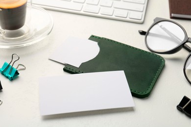 Leather business card holder with blank cards, glasses, keyboard and stationery on white table, closeup