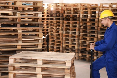 Image of Worker moving wooden pallets with manual forklift in warehouse