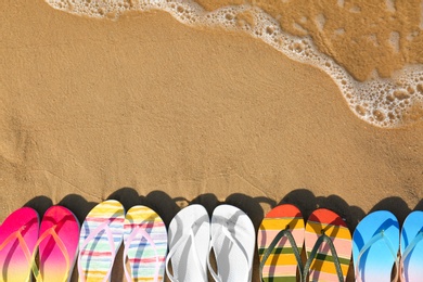 Photo of Flat lay composition with flip flops on sand near sea, space for text. Beach accessories