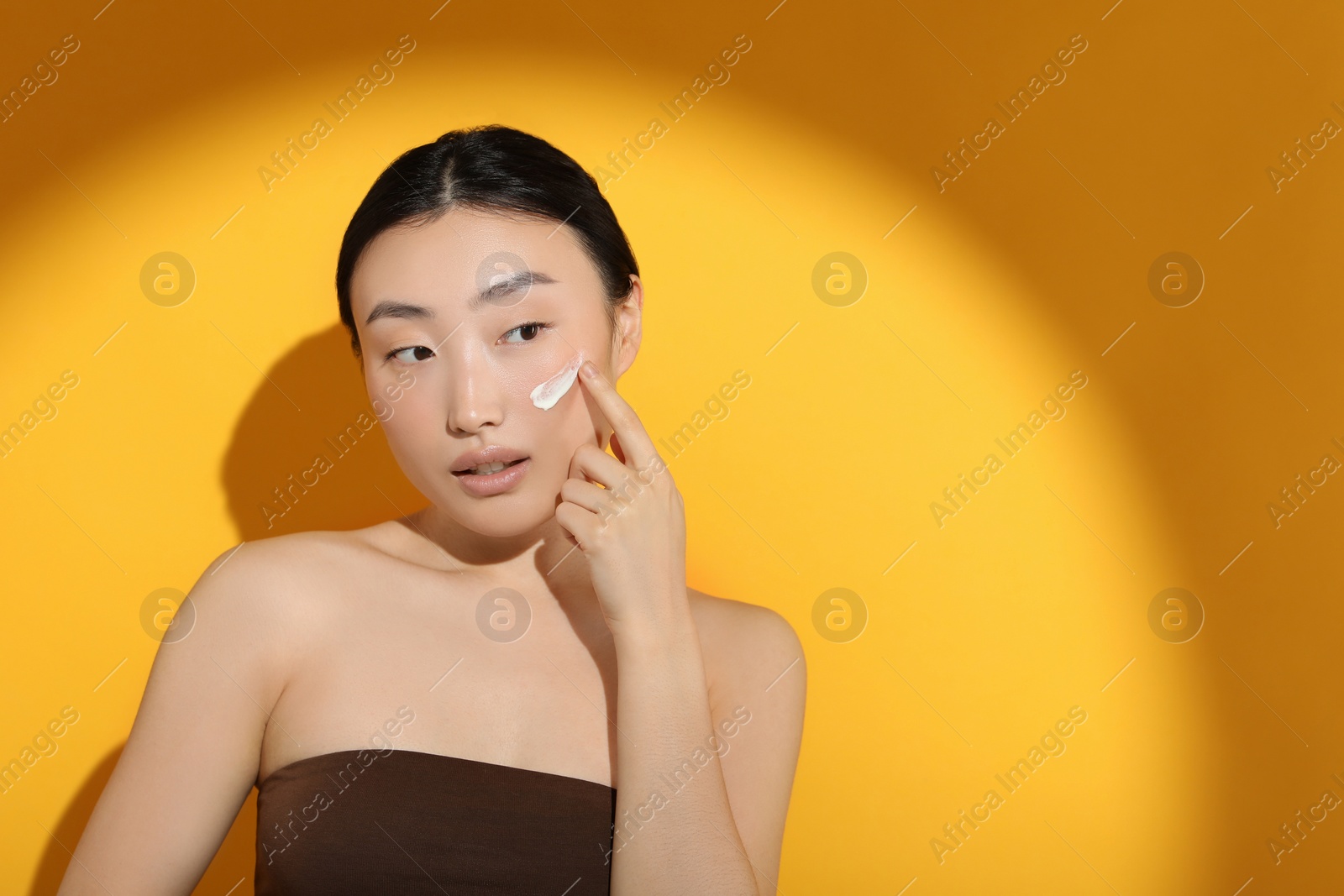 Photo of Beautiful young woman in sunlight with sun protection cream on her face against orange background, space for text