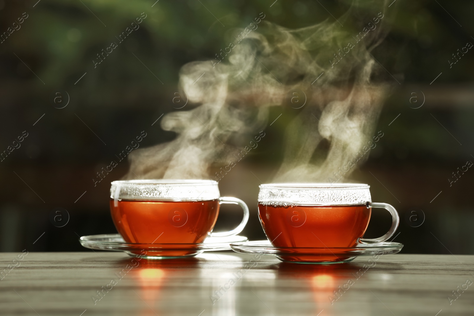 Photo of Cups of hot tea on wooden table against blurred background, space for text