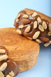 Photo of Supreme croissants with chocolate paste and nuts on light blue background, closeup. Tasty puff pastry