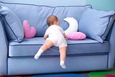 Photo of Cute baby climbing on couch in living room