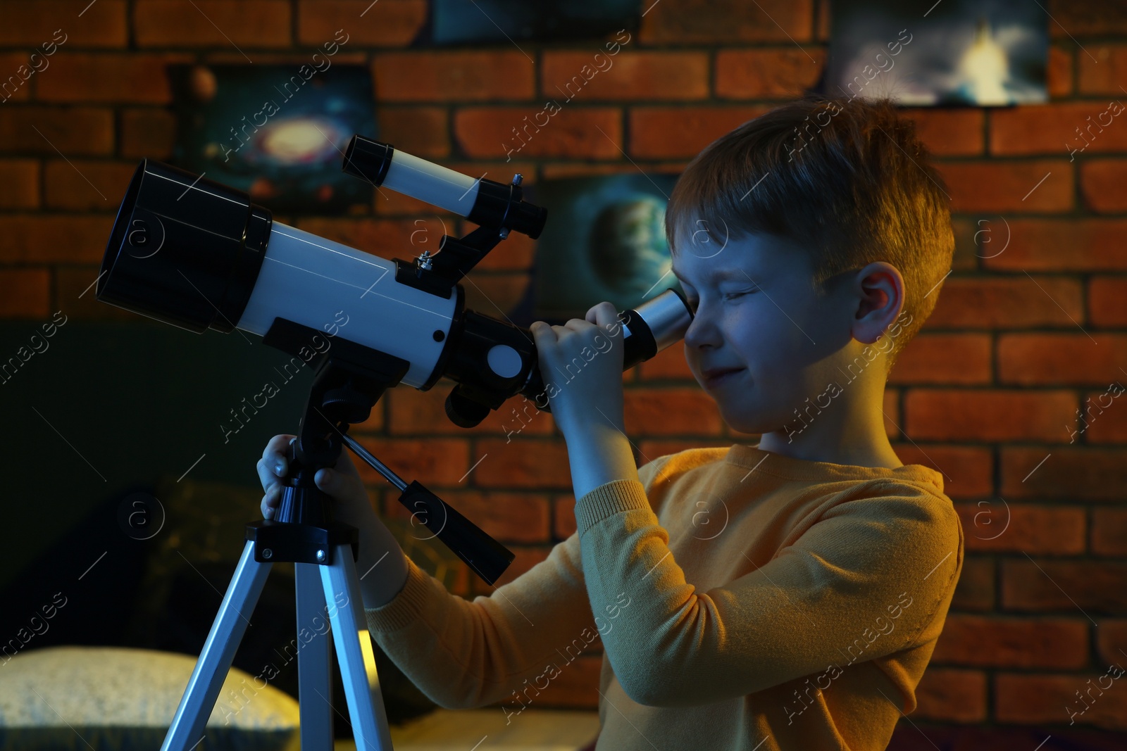 Photo of Little boy looking at stars through telescope in room