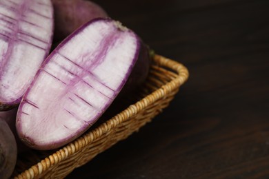 Photo of Purple daikon radishes in wicker basket on wooden table, closeup. Space for text