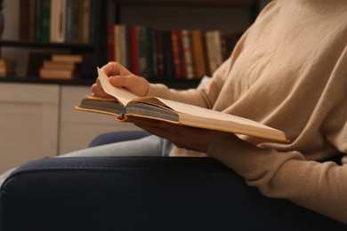 Photo of Young woman reading book in home library, closeup