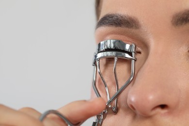 Woman using eyelash curler on white background, closeup. Space for text